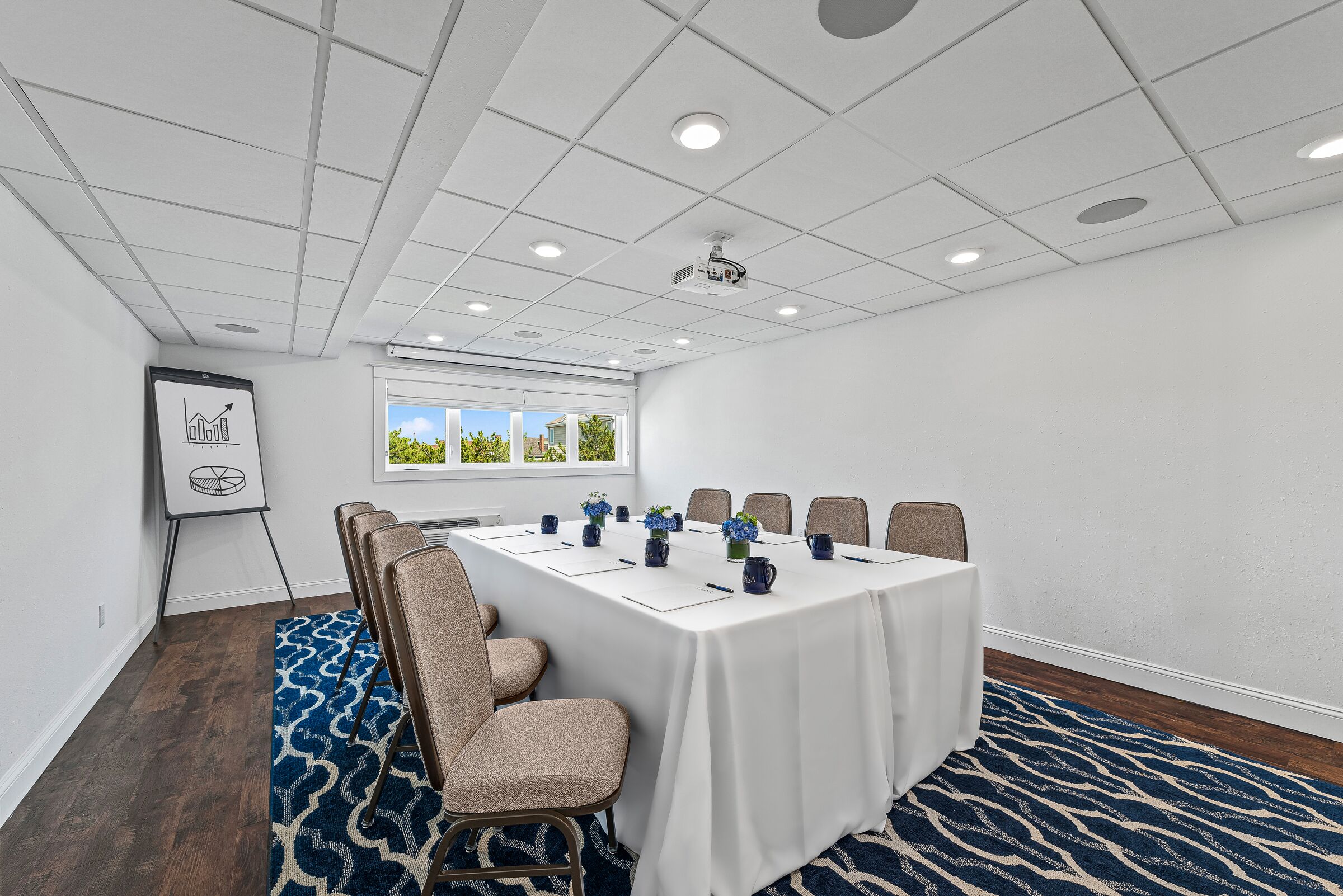 A conference room with a white table, beige chairs, a projector, and a presentation screen.