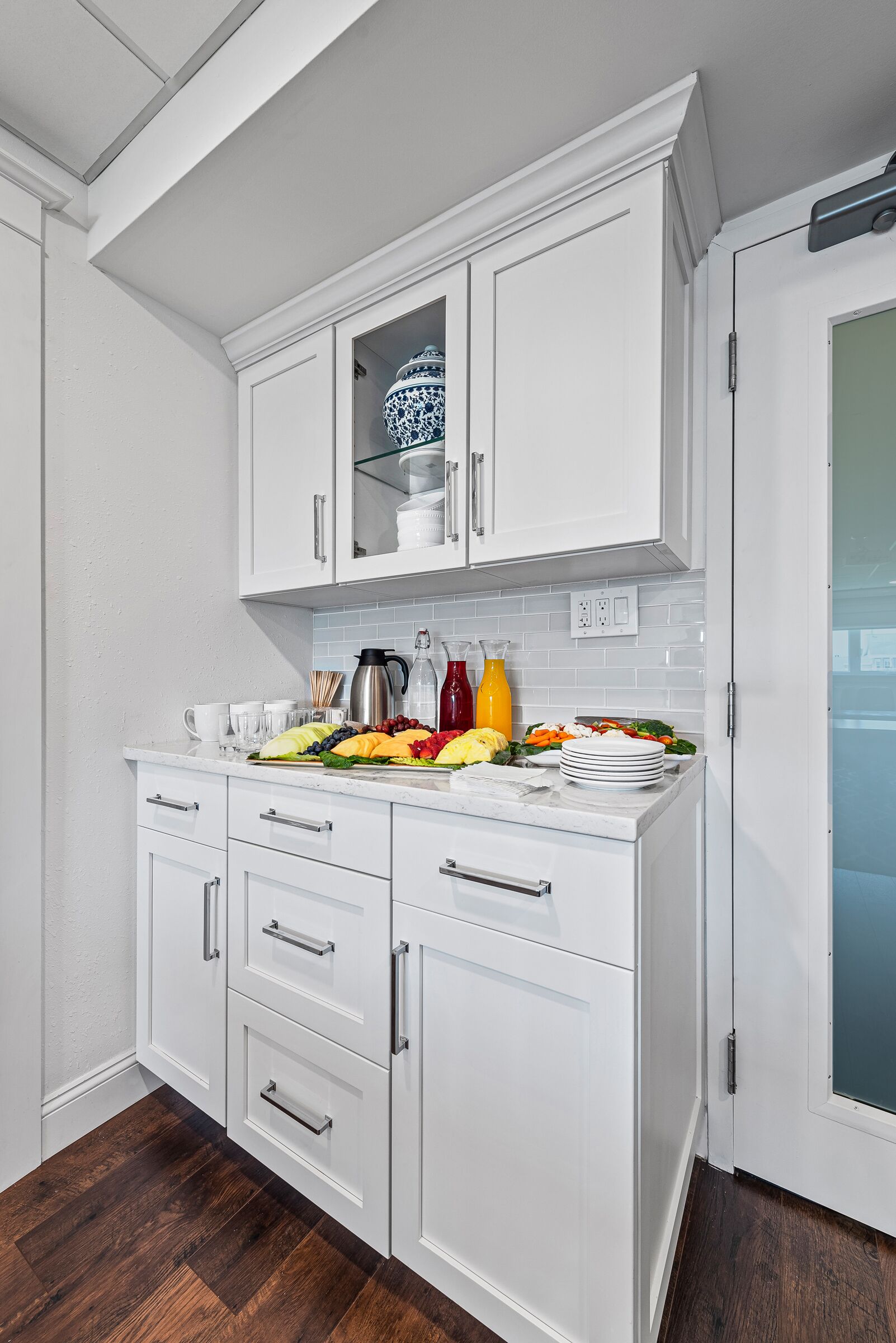 A kitchen with white cabinets, a marble countertop, and a variety of fruits and vegetables.