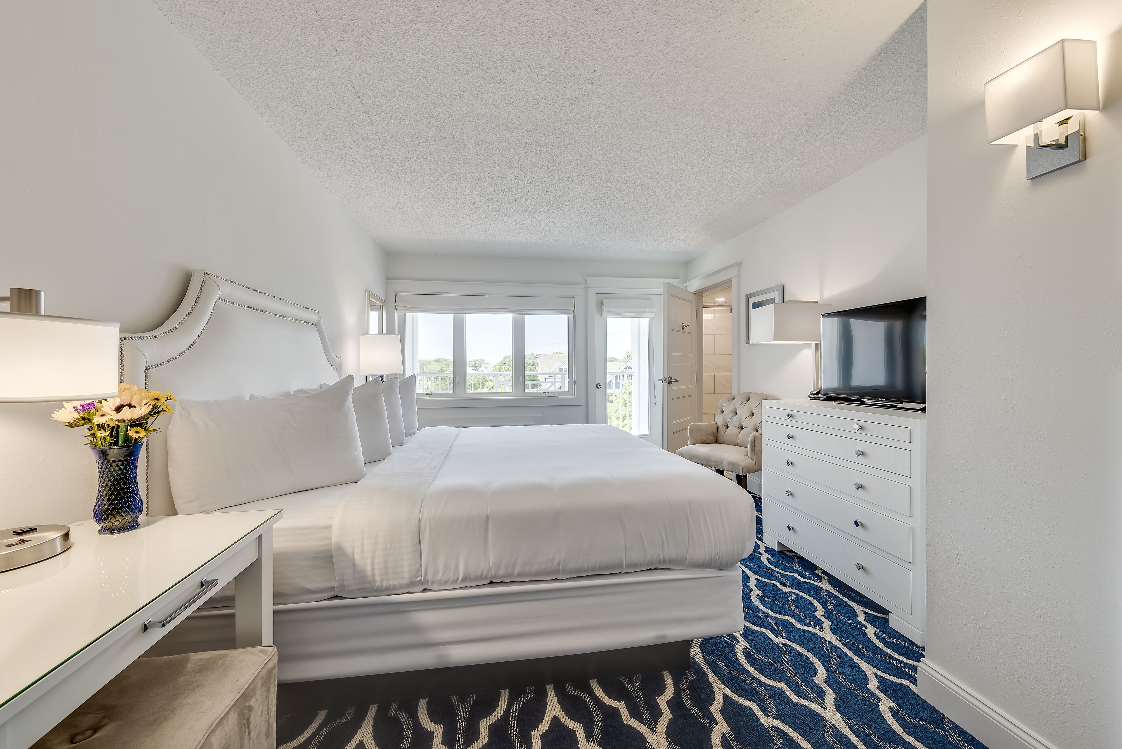 A hotel room with a bed, a desk, a dresser, a TV, and a window.