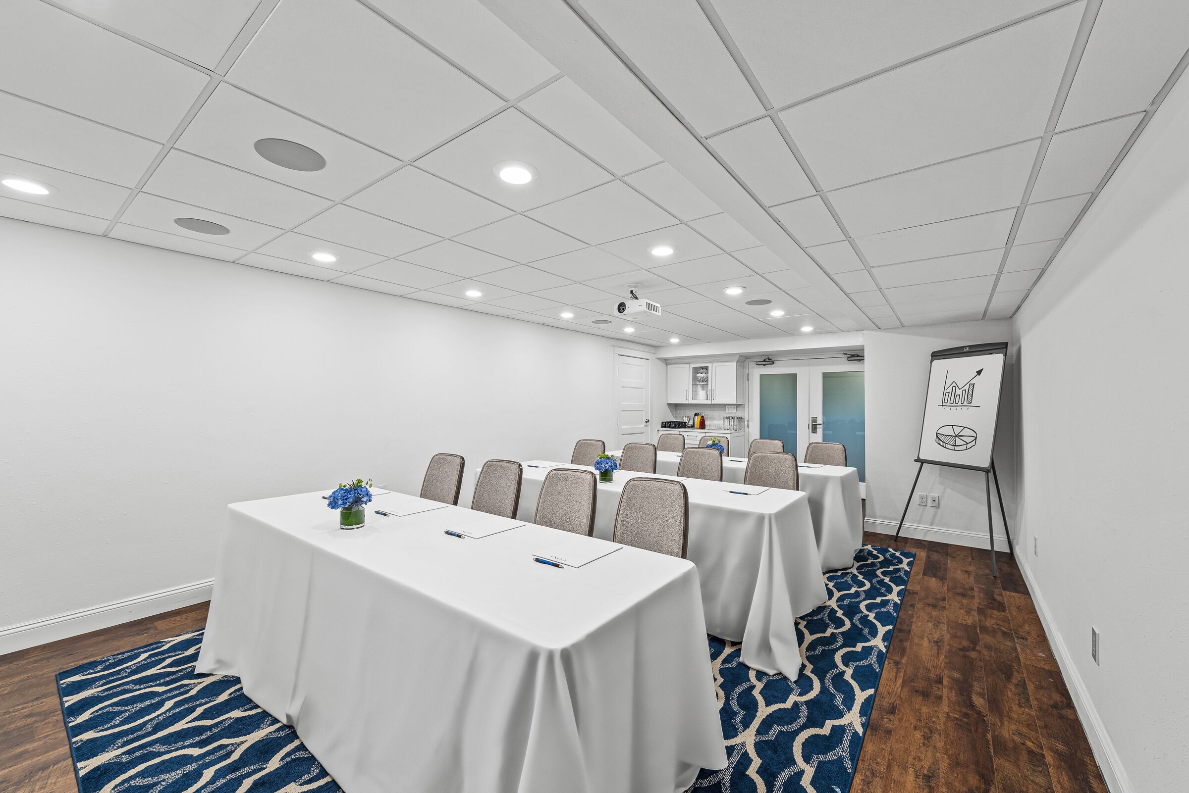 Une salle de conférence avec des tables et des chaises blanches, et un projecteur fixé au plafond.