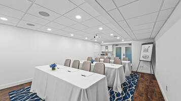 Une salle de conférence avec des tables et des chaises blanches, et un projecteur fixé au plafond.