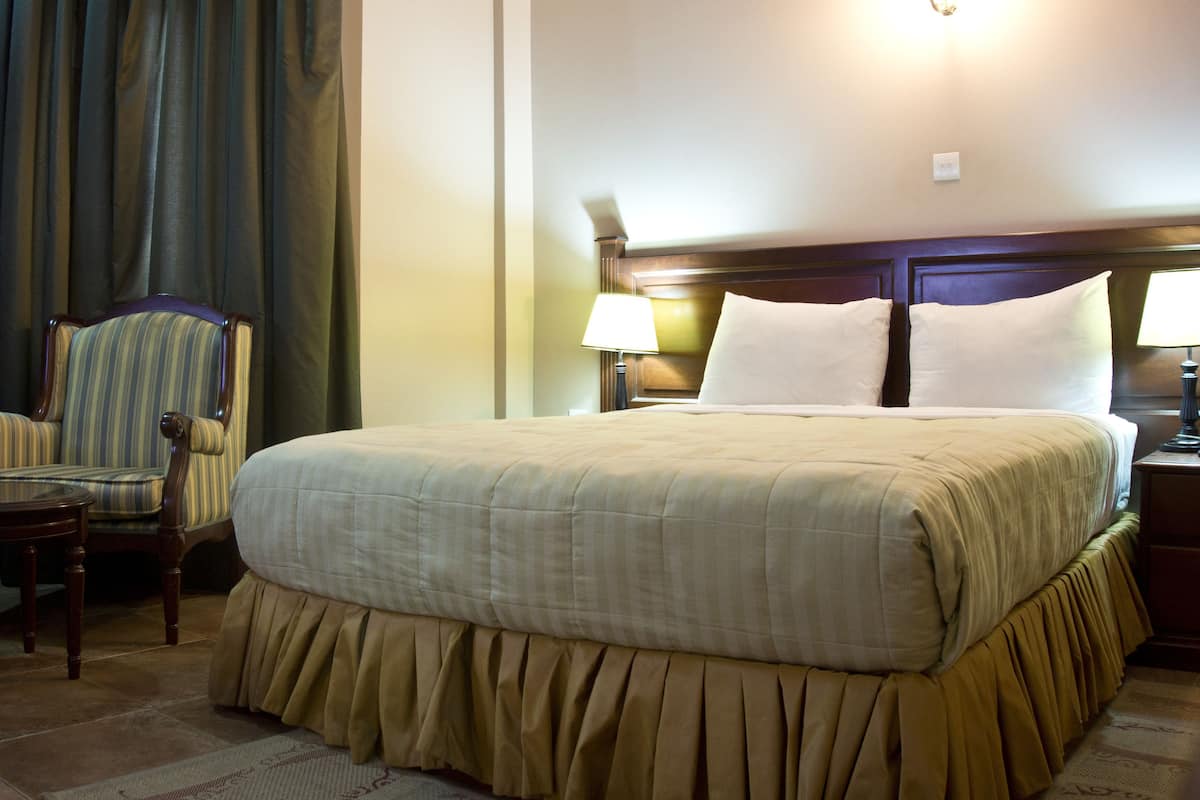 A hotel room with a large bed, a chair, a small table, and a lamp.