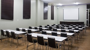 Une salle de conférence avec des rangées de tables et de chaises, un écran de projection et des appareils de climatisation.