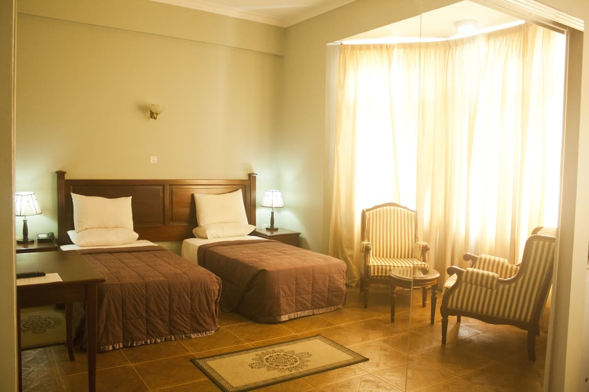 A hotel room with two single beds, a desk with a lamp, a chair, and a small table.
