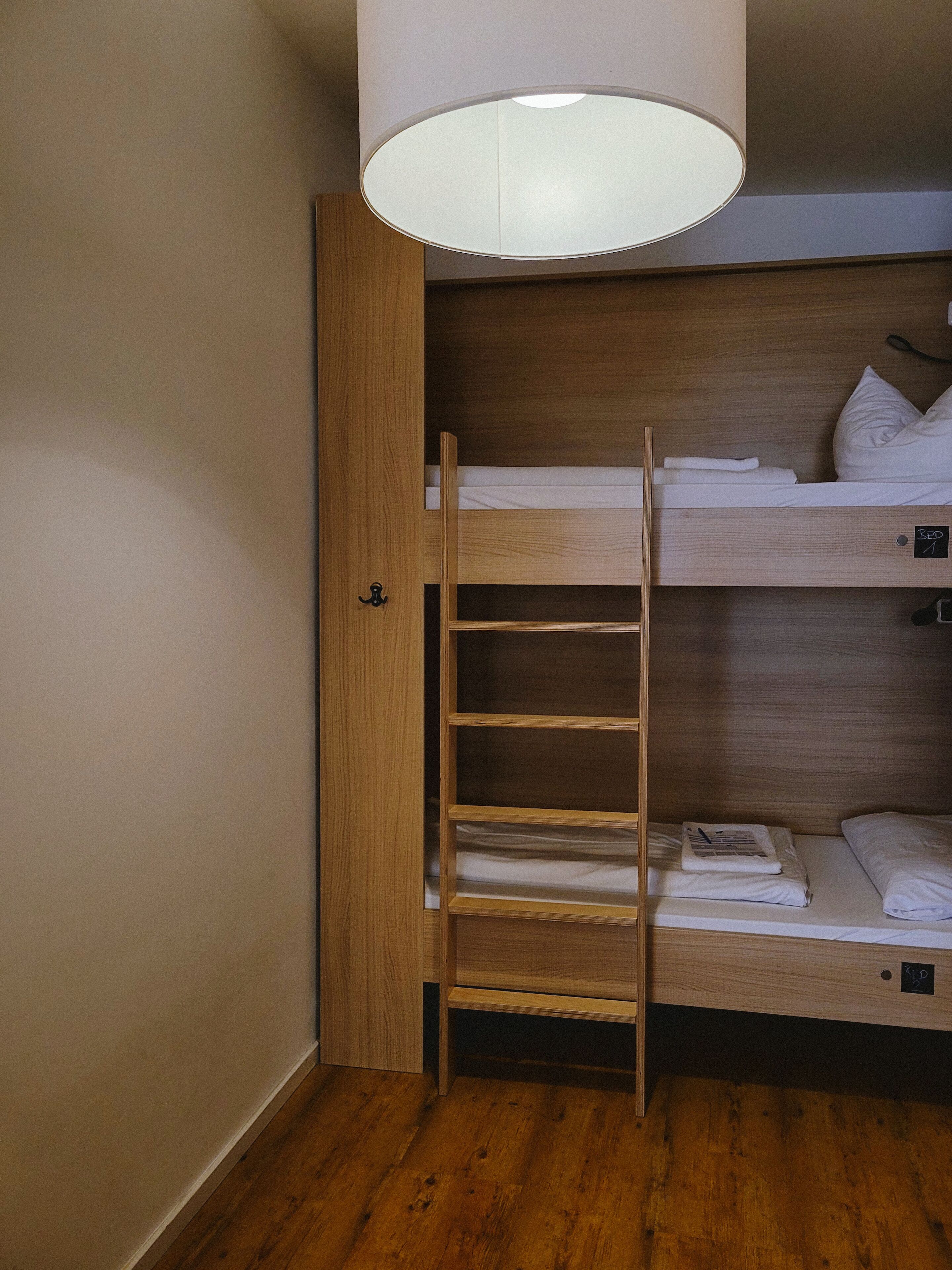 A bunk bed with a wooden ladder, a small shelf, and a hanging light fixture.