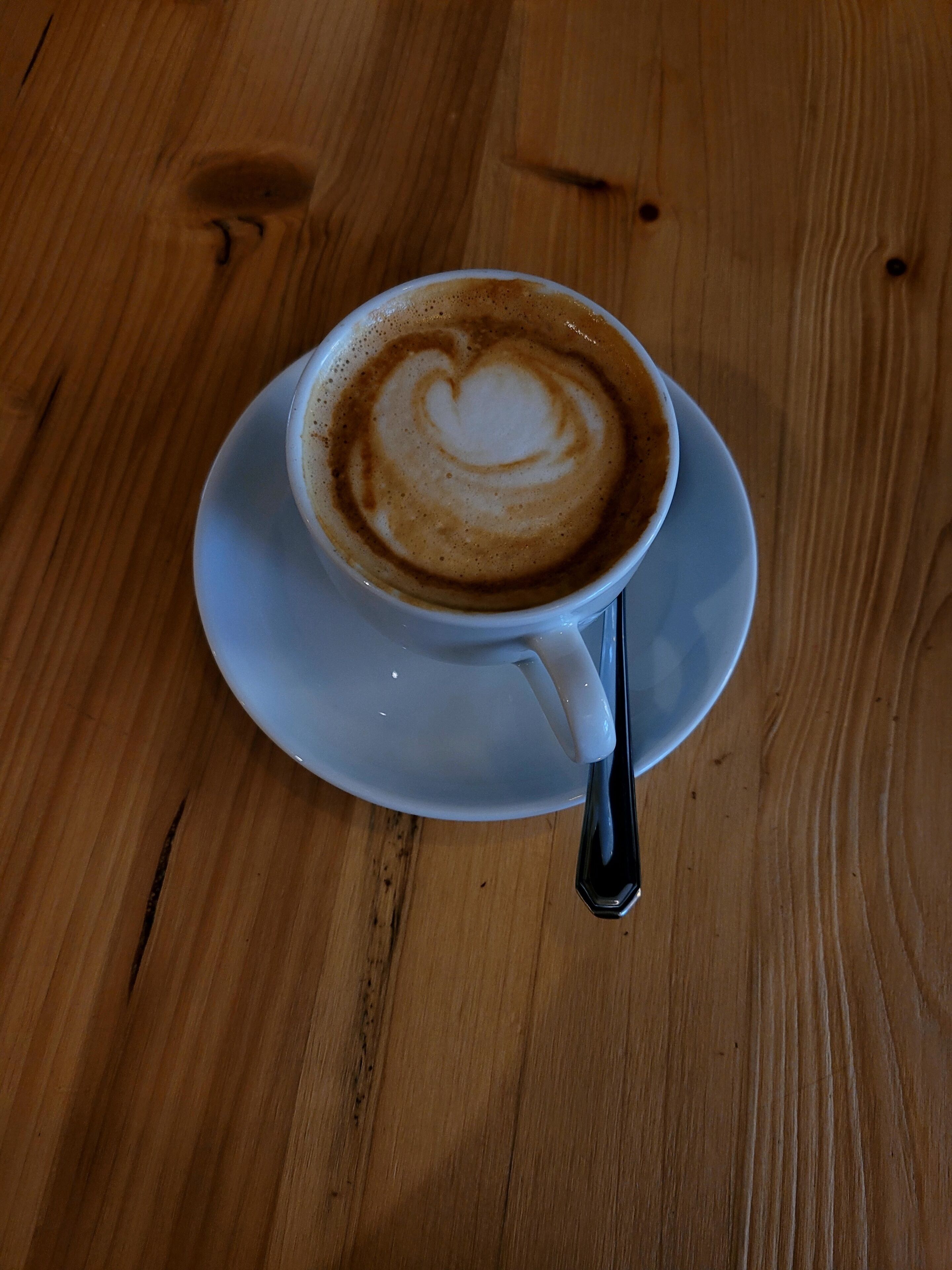 Uma chávena de café com arte de latte em formato de coração sobre uma mesa de madeira.