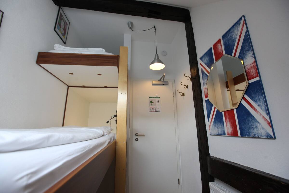 Een kleine kamer met een stapelbed, een nachtkastje, een spiegel en een kunstwerk aan de muur.