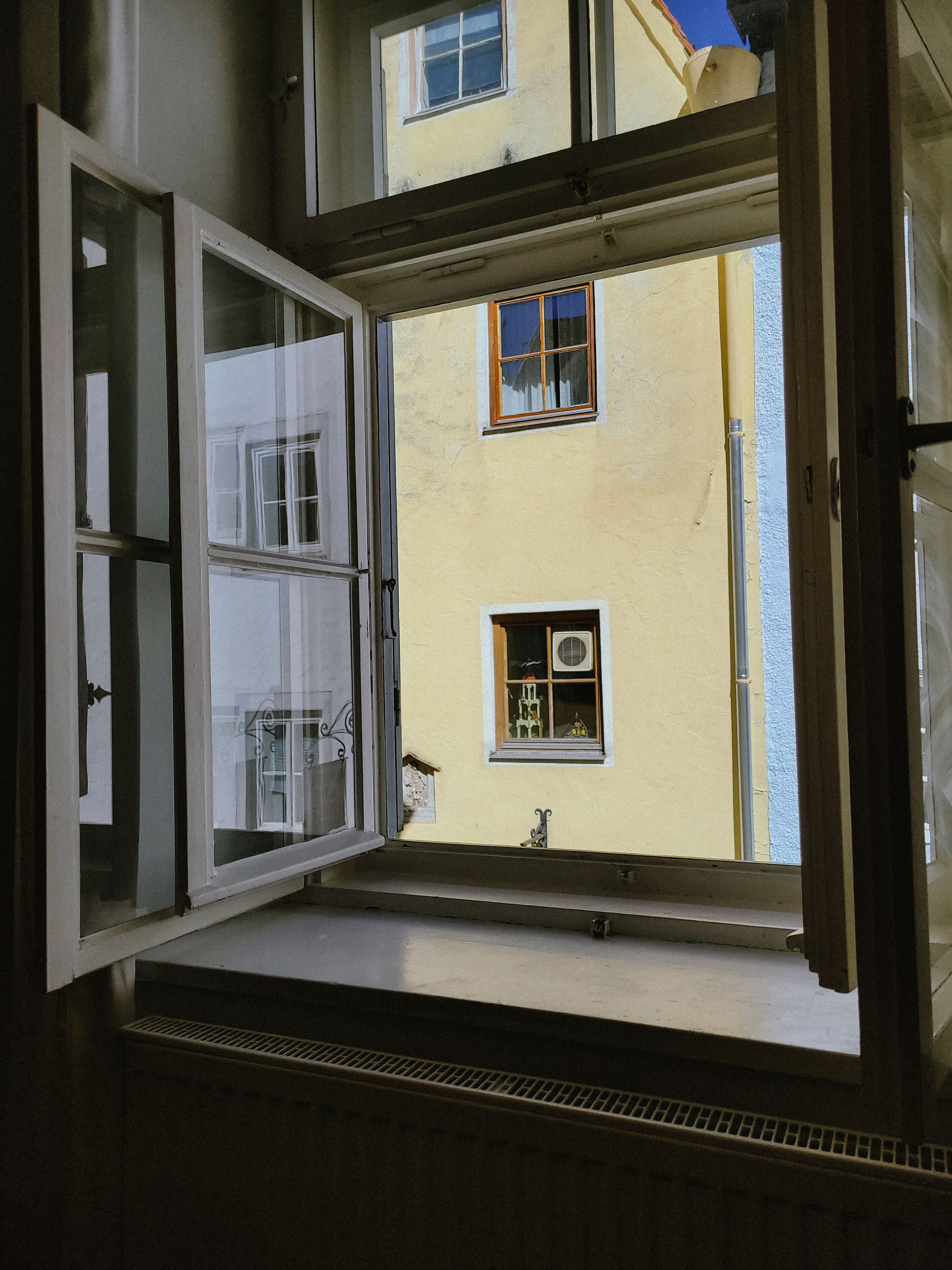 An open window with a view of a building with multiple windows and a vent.