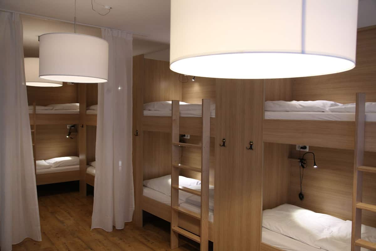 Een slaapkamer met stapelbedden, houten wanden, witte beddengoed en hanglampen.