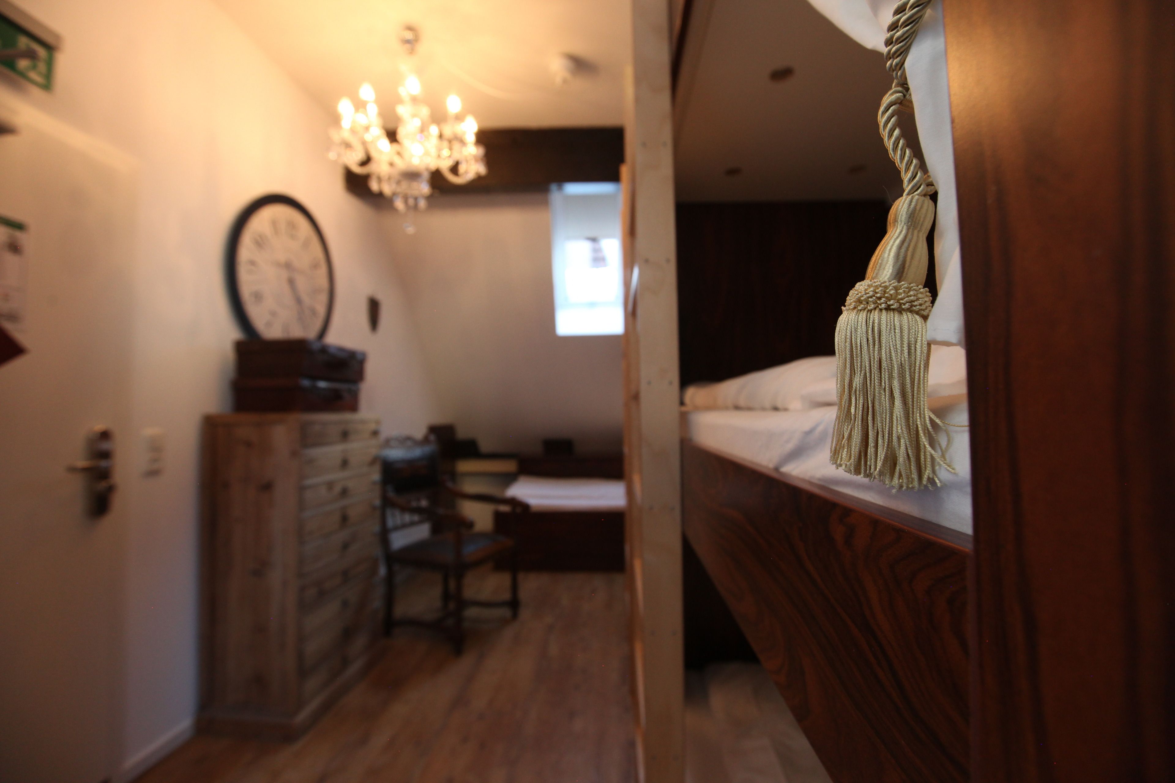 A bedroom with a wooden headboard, a bed with white bedding, a chandelier, a clock, and a wooden dresser.