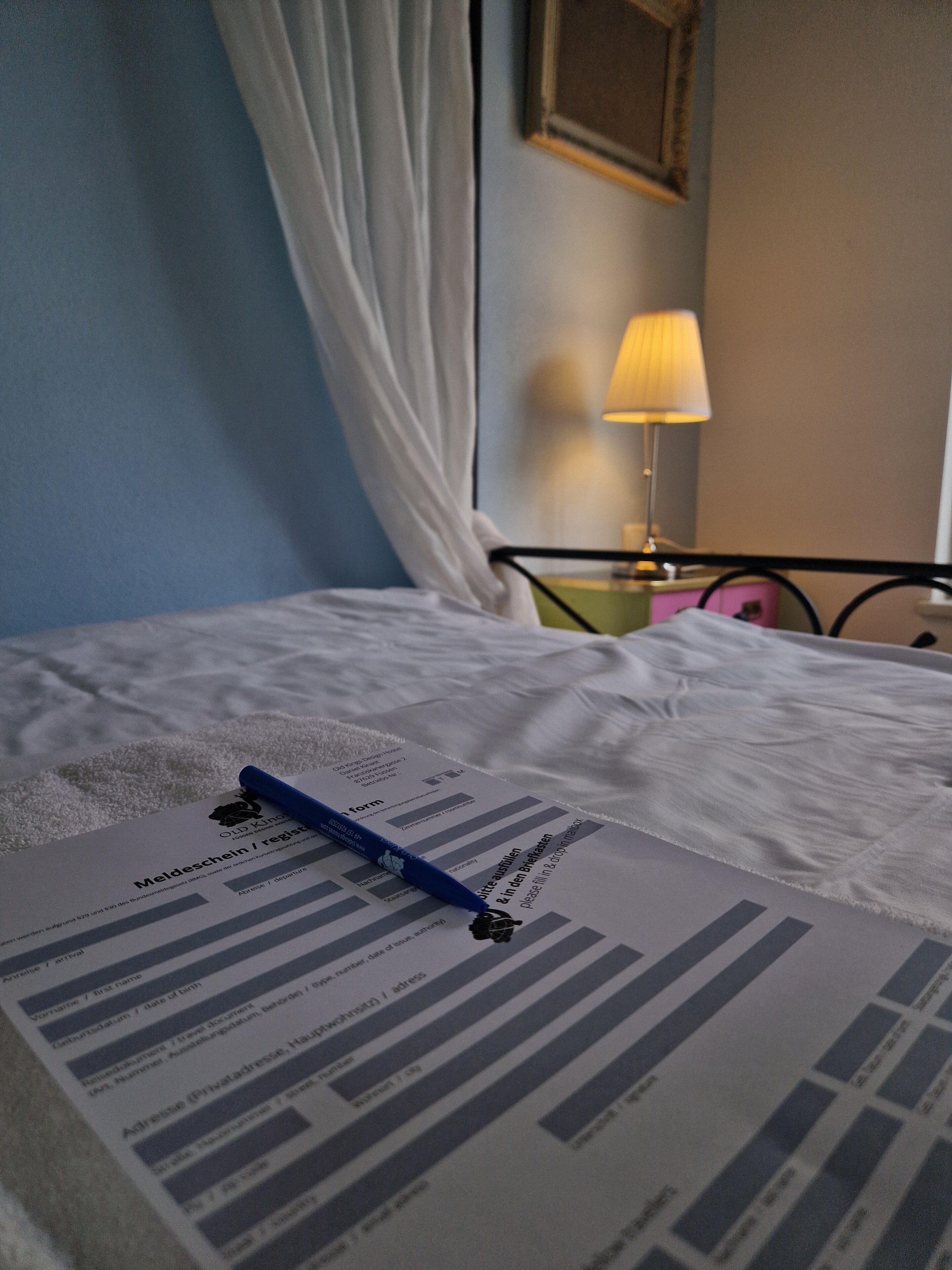 A bed with a form and pen on it, a lamp, and a curtain.