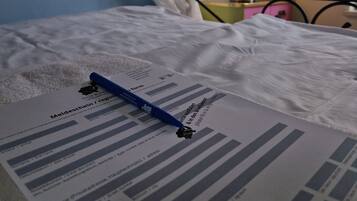 A bed with a form and pen on it, a lamp, and a curtain.