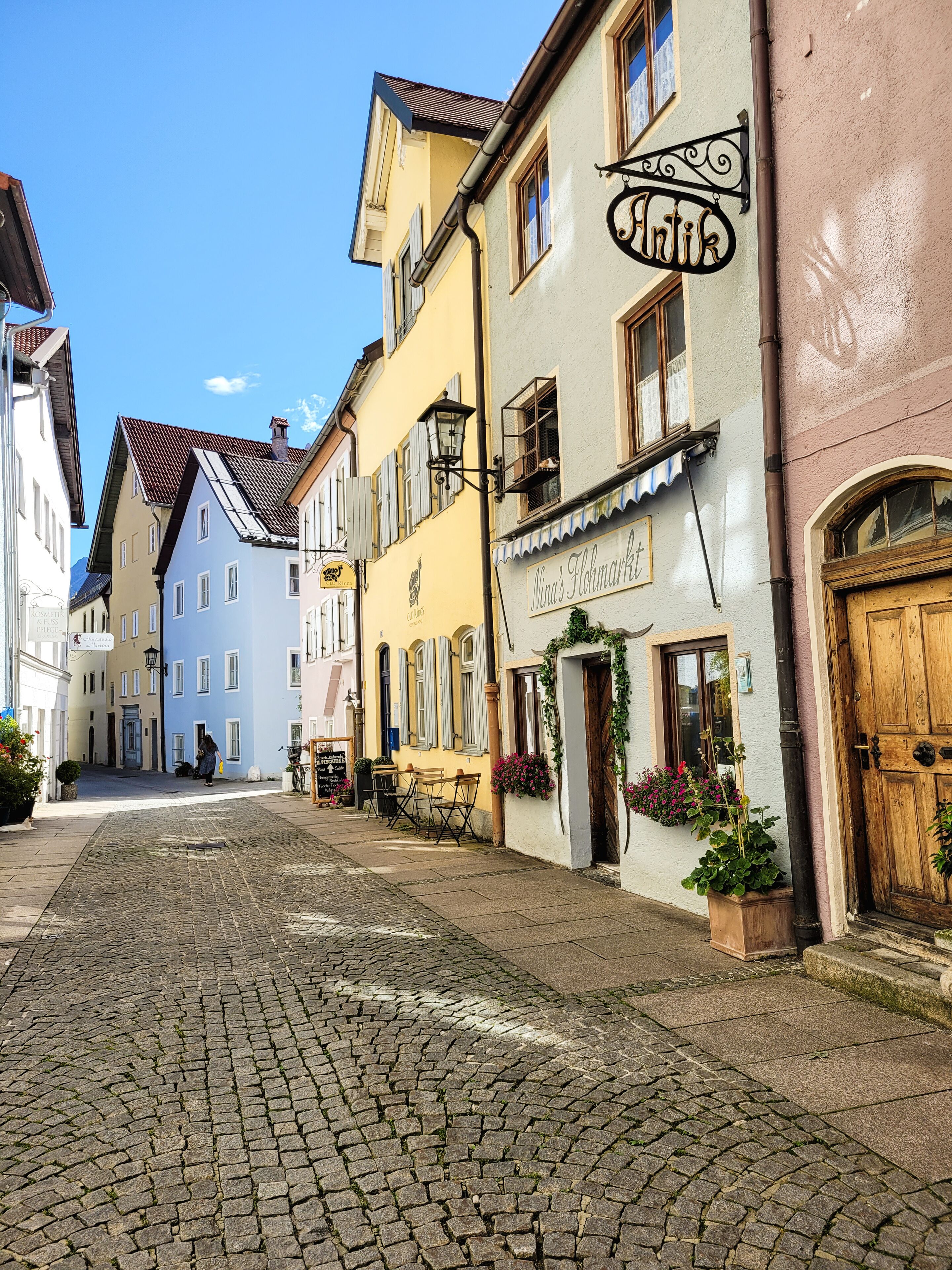 A cobblestone street lined with colorful buildings, including a restaurant named "Nina's Floremarkt" with outdoor seating.