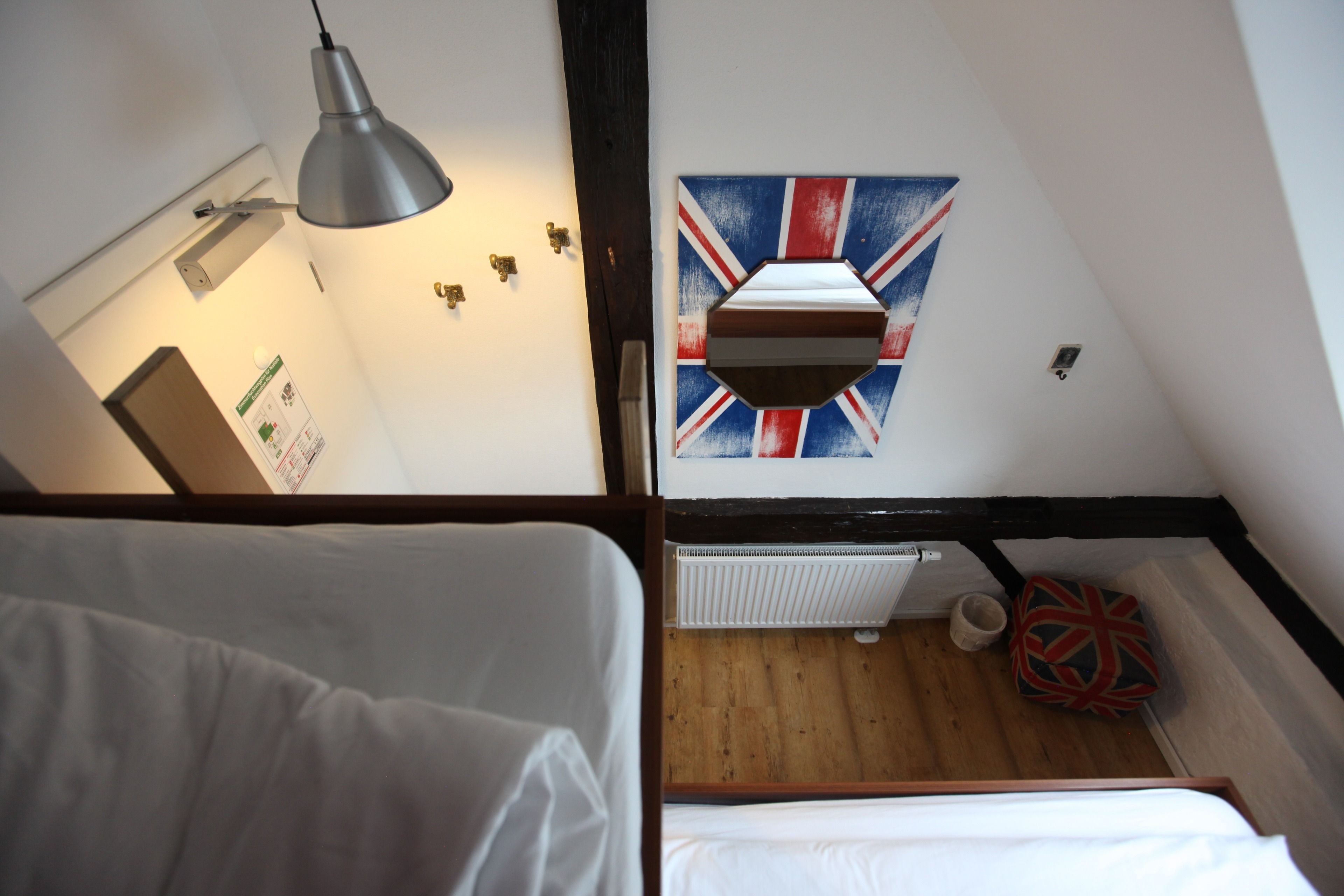 A room with a bed, a hanging lamp, a radiator, and a wall with a Union Jack flag.
