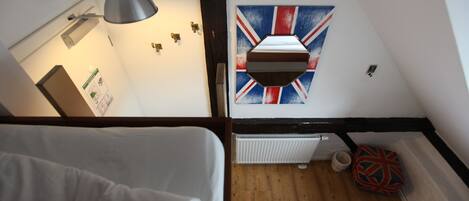 A room with a bed, a hanging lamp, a radiator, and a wall with a Union Jack flag.
