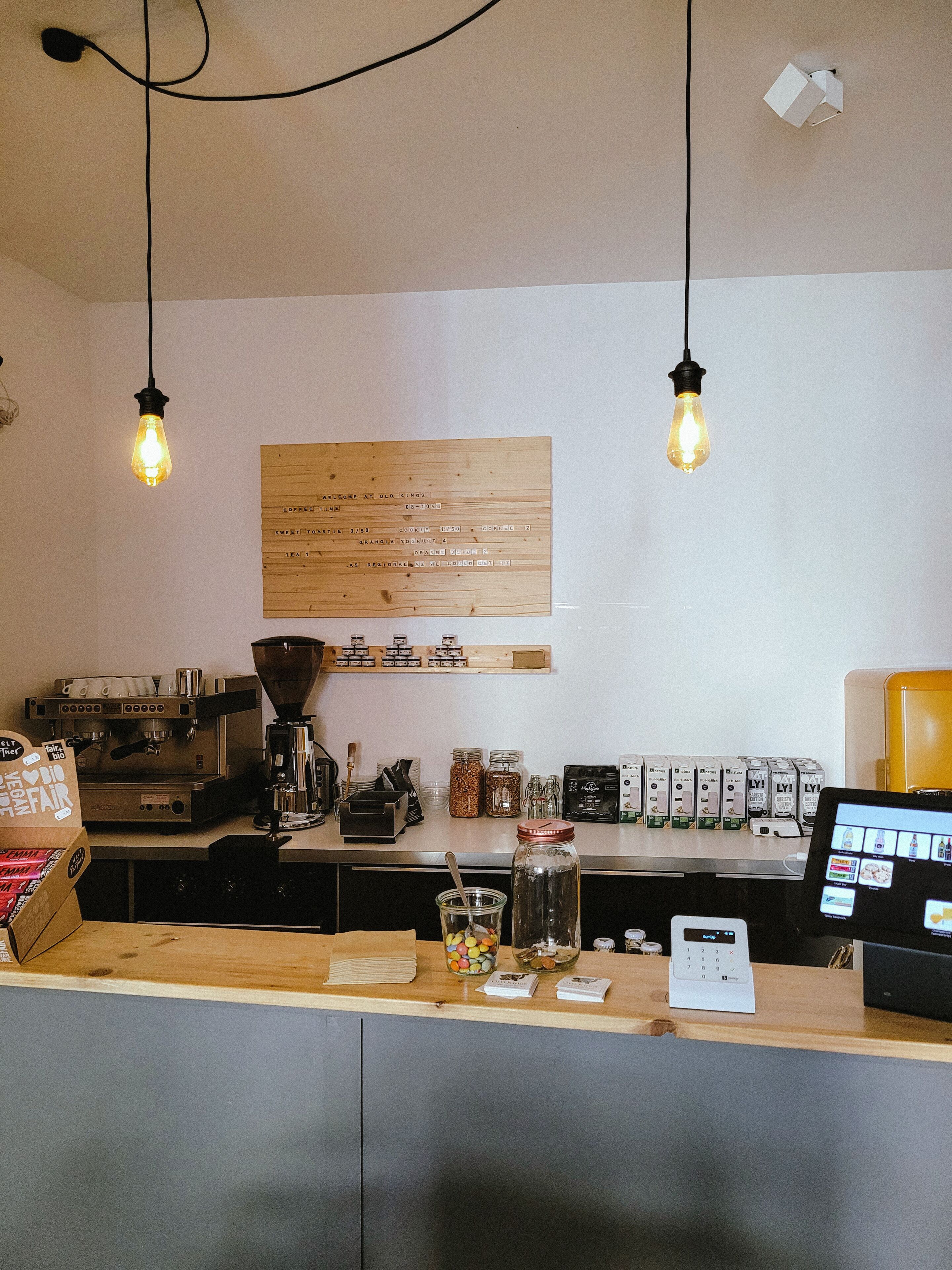 A coffee shop counter with an espresso machine, a menu board, and a digital payment terminal.