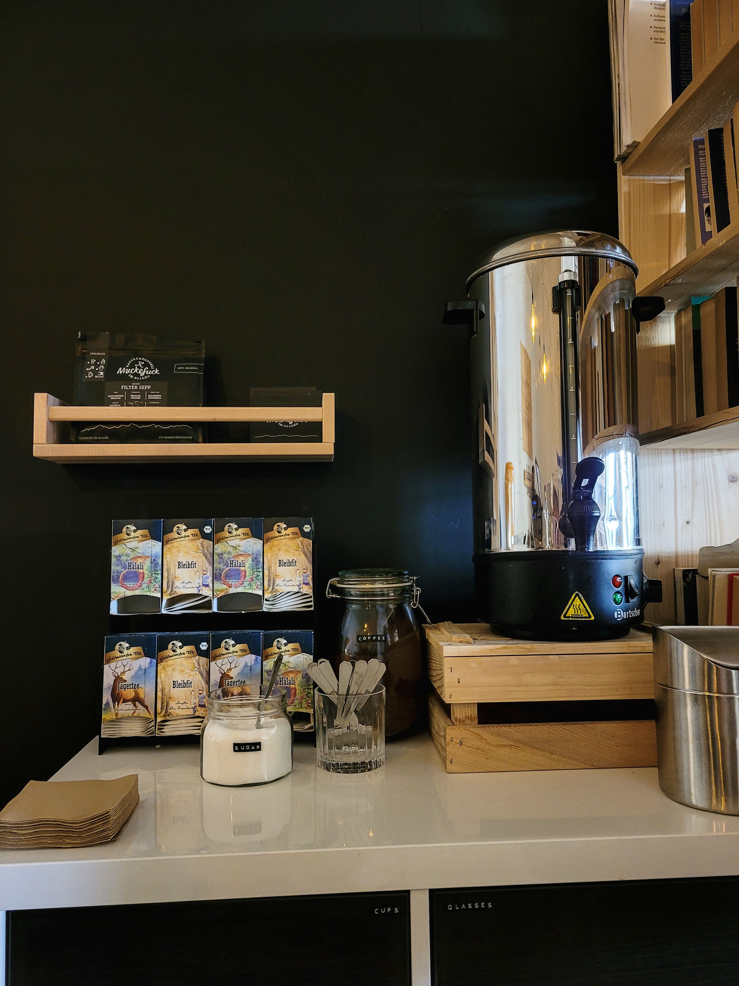 Una encimera de cocina con una cafetera, un tarro de azúcar y sobres de café.