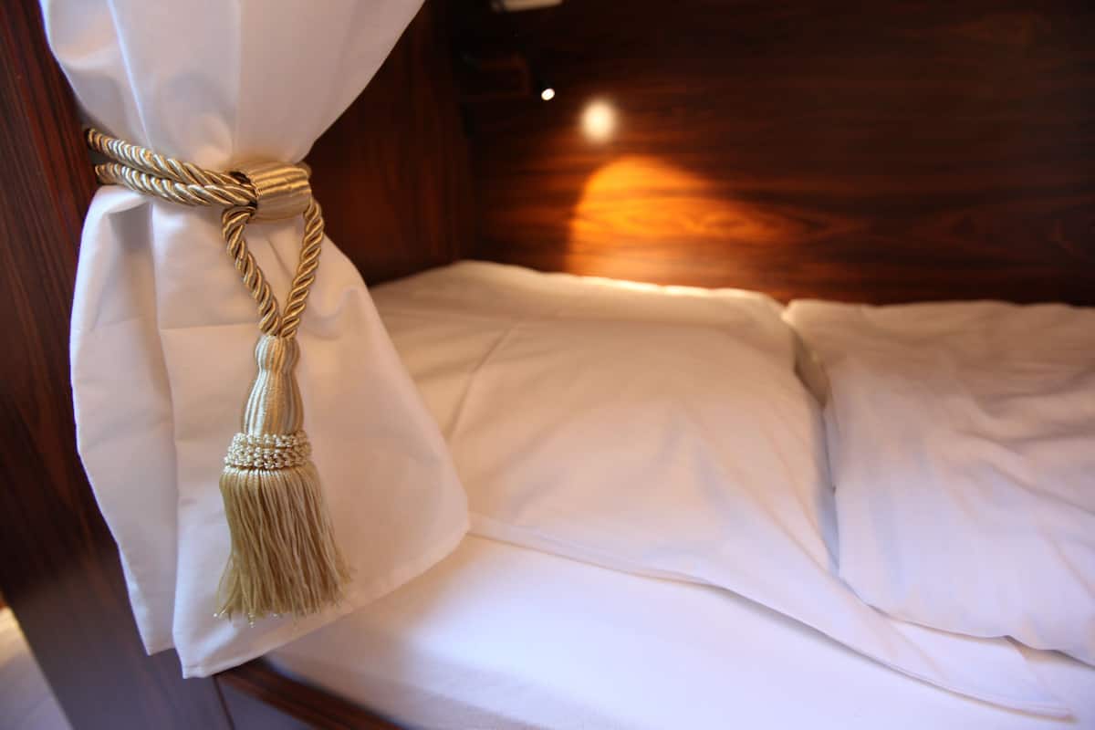 Een net opgemaakt bed met witte lakens en een decoratieve kwast aan de gordijn.