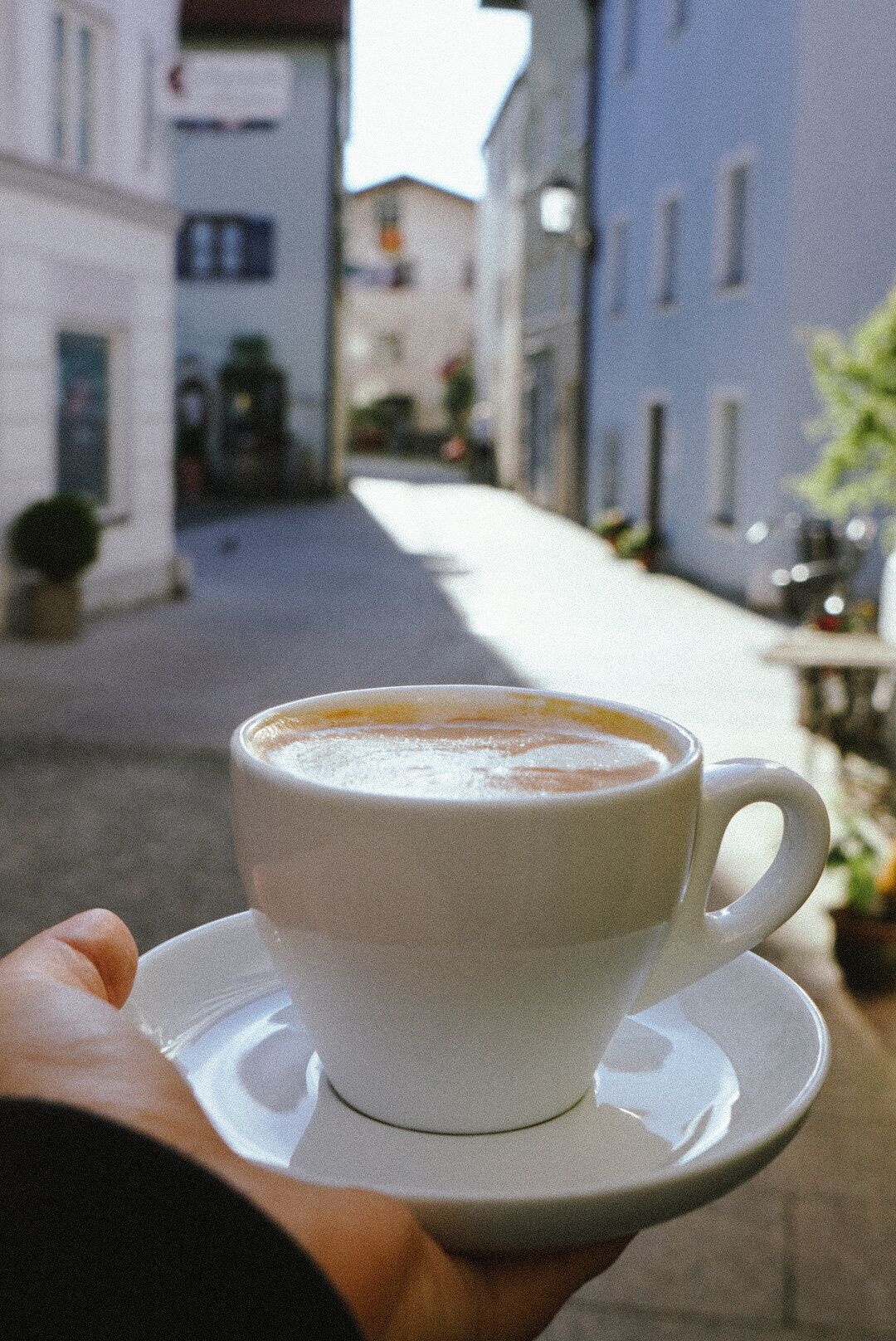 Uma chávena de café sobre um pires, segurada por uma pessoa.
