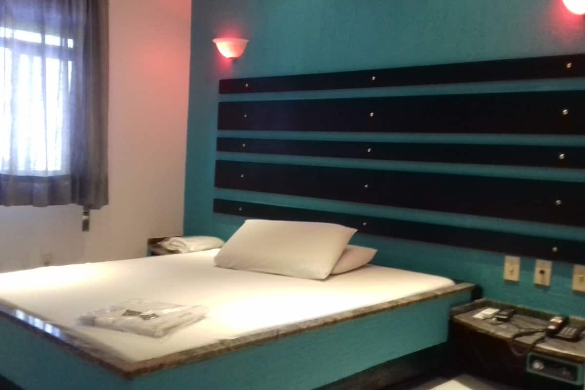 Una habitación de hotel con una cama, una mesita de noche, una lámpara y un aplique de pared.