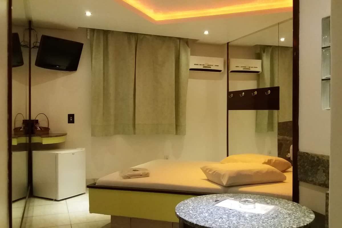 Habitación de hotel pequeña con cama, mesita de noche, televisor montado en la pared y equipo de aire acondicionado.