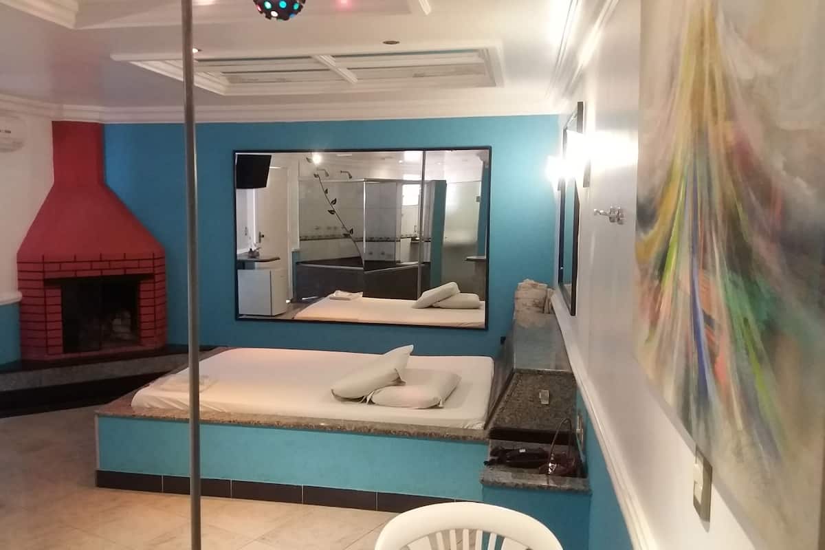 Un dormitorio con cama, chimenea, un espejo grande y un baño visible a través de una puerta de cristal.