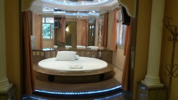 A circular bed in a luxurious bathroom with a mirror, a sink, and a shower. - Motel dos Arcos (Porto Alegre)