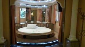 Una cama redonda en un baño lujoso con un espejo, un lavamanos y una ducha.