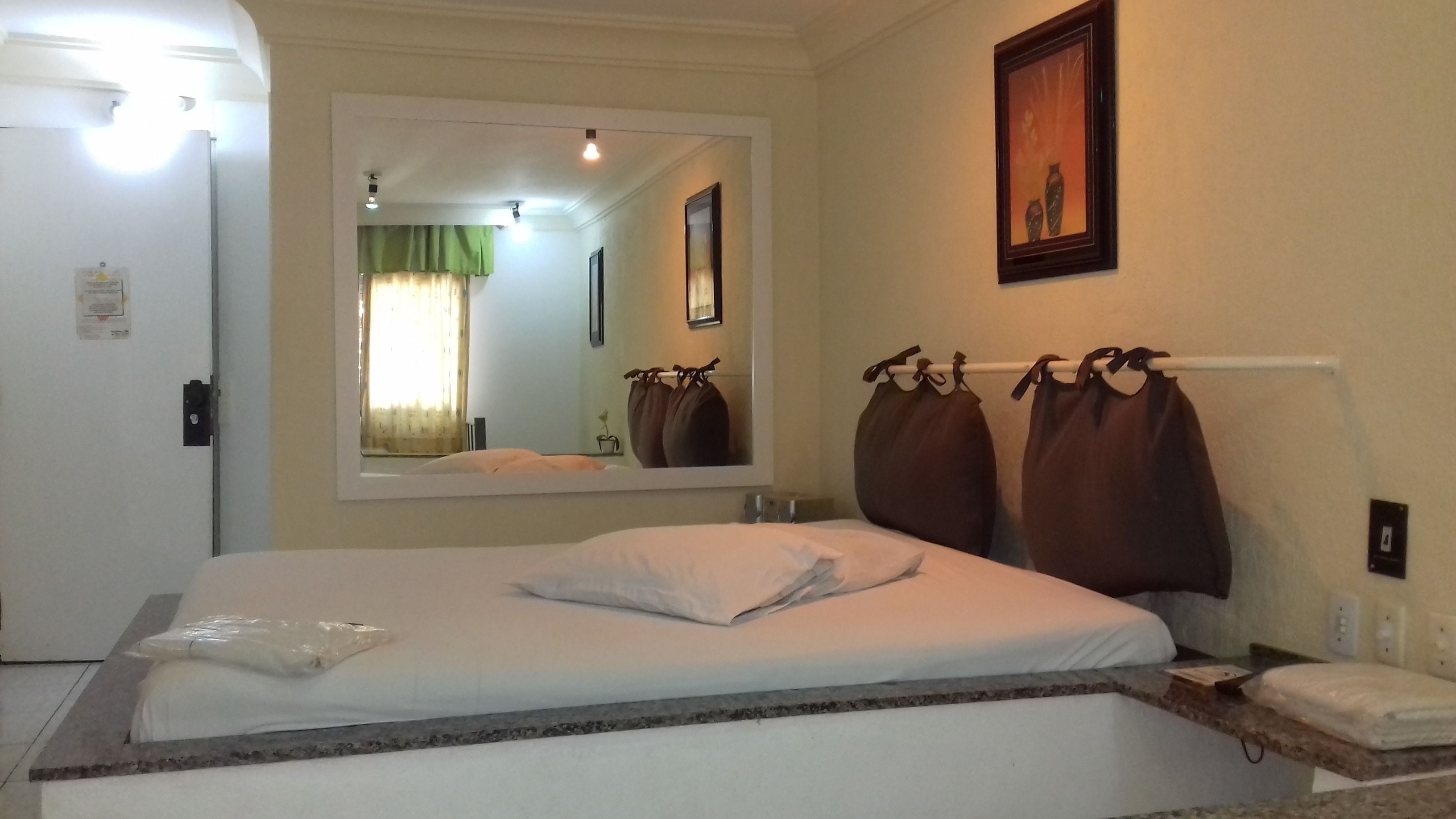 Habitación de hotel con una cama grande, una mesita de noche, un espejo y un cuadro en la pared.