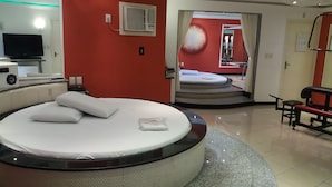 A modern hotel room with a circular bed, a TV, and a red wall with a fruit mural. - Motel dos Arcos (Porto Alegre)