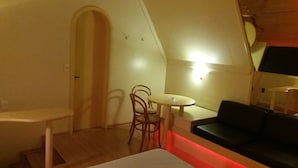 A small, cozy room with a round table, a single chair, a sofa, and a staircase leading to an upper level. - Motel dos Arcos (Porto Alegre)