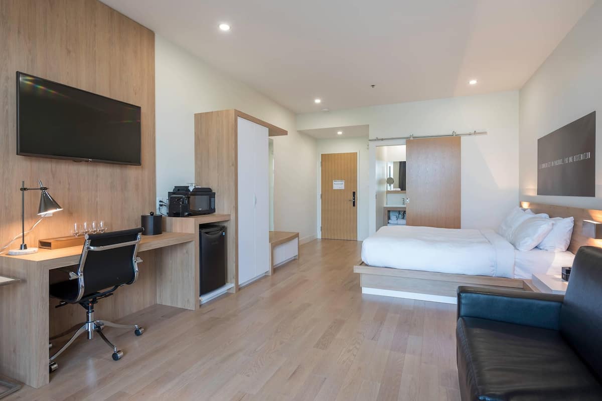 Een moderne hotelkamer met een flatscreen televisie, een bureau met een computer, een bed, een sofa en een badkamer.