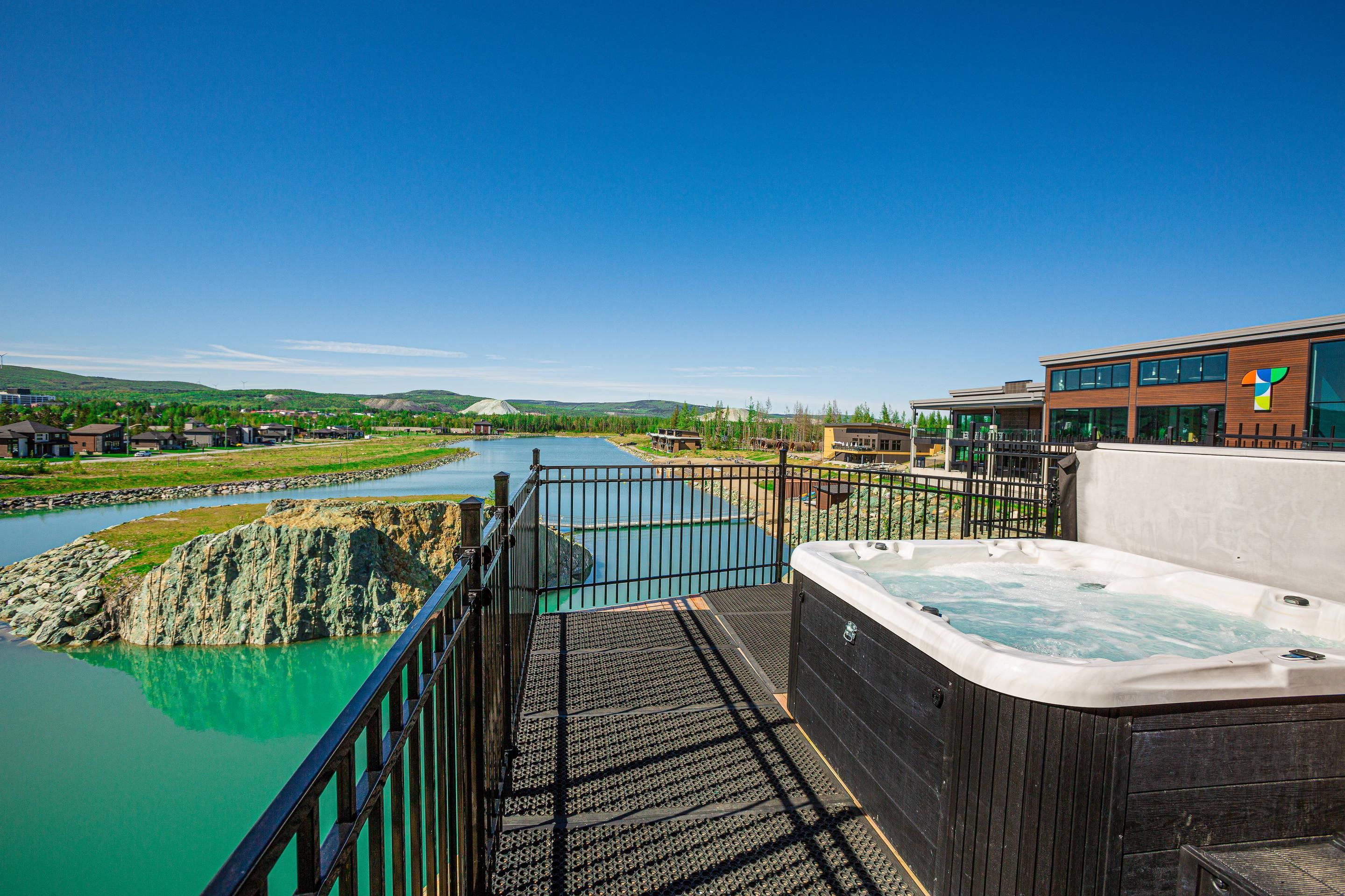 Un bain à remous sur une terrasse donnant sur une rivière, avec un bâtiment en arrière-plan.