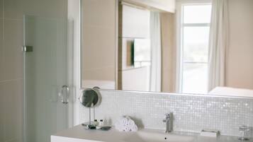 A modern bathroom with a large mirror, white tiles, a sink, and a glass shower enclosure.