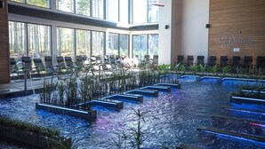 Un hall d’hôtel doté d’une grande piscine intérieure, de rangées de fauteuils et offrant une vue sur une forêt à travers de grandes fenêtres.
