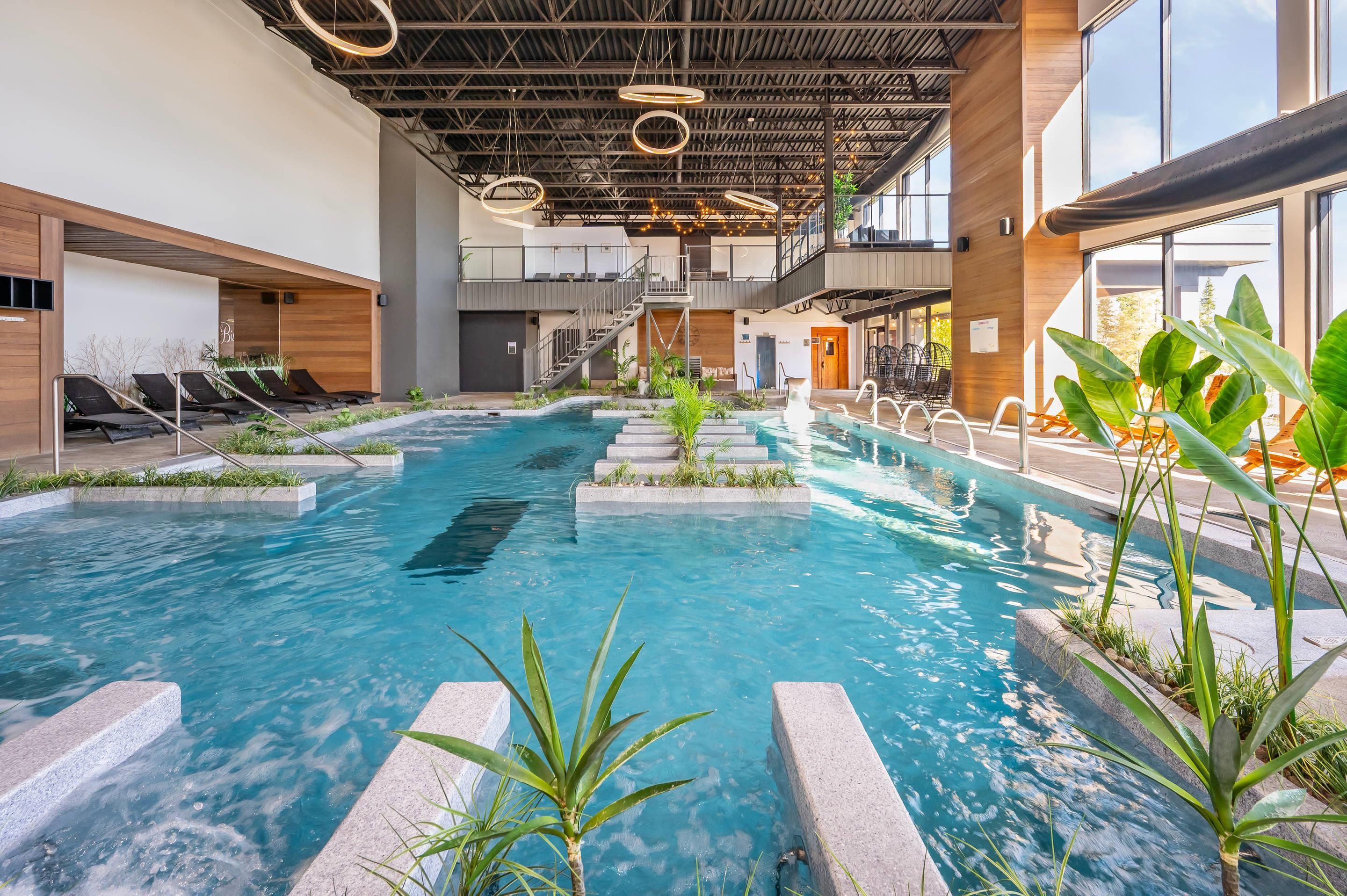 An indoor swimming pool with a modern design, surrounded by lounge chairs and plants.