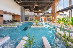 An indoor swimming pool with a modern design, surrounded by lounge chairs and plants. - Hotel du Domaine, an Ascend Collection Hotel (Thetford Mines)