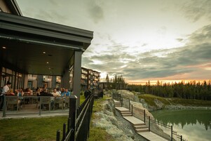 Un edificio moderno con mesas al aire libre que ofrece vistas a un lago tranquilo y un área boscosa.