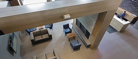 A modern hotel lobby with a high ceiling, wooden beams, and a seating area with sofas and tables.