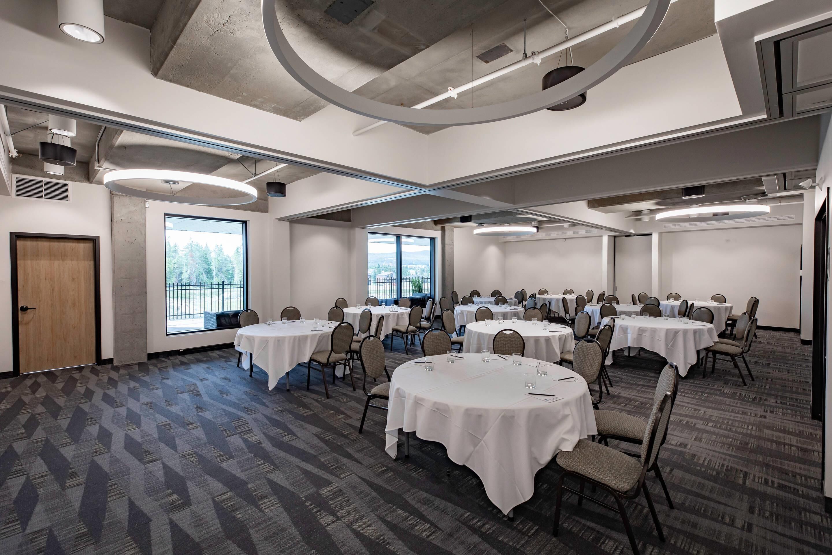 A conference room with round tables, chairs, and large windows offering a view of the outdoors.