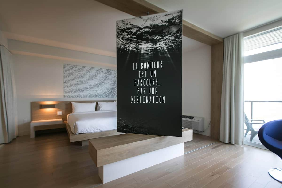 Een moderne hotelkamer met een bed, nachtkastje en een groot raam.