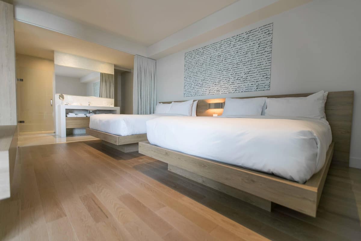 Een moderne hotelkamer met een groot bed, een kleiner bed, een kaptafel met spiegel en een kunstwerk aan de muur.