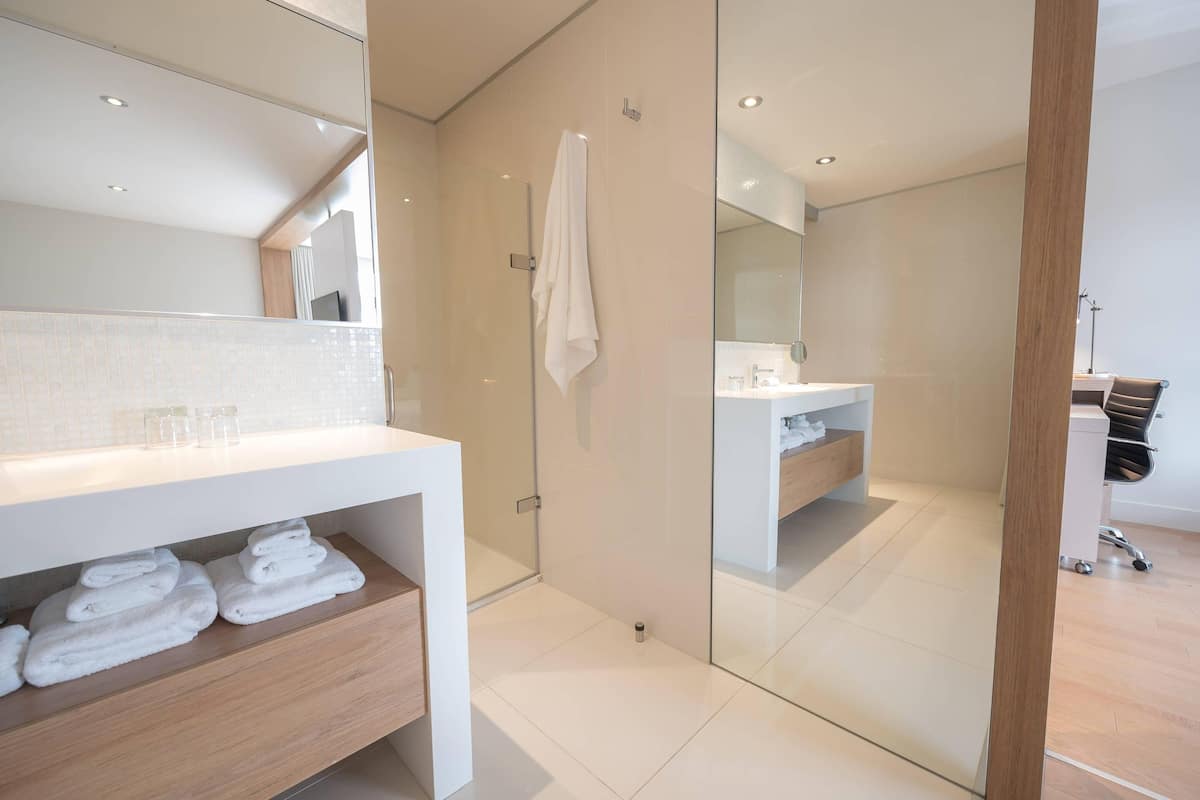 Een moderne badkamer met een douchecabine van glas, een witte wastafel en netjes opgevouwen handdoeken.