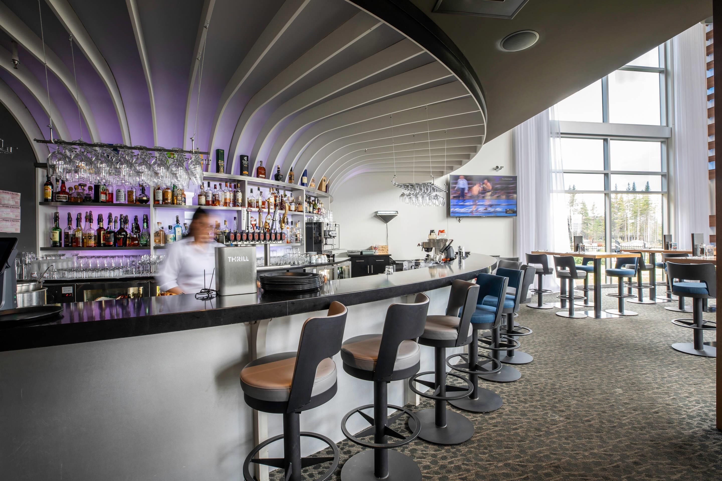 A bar area with a curved ceiling, bar stools, and a bartender.
