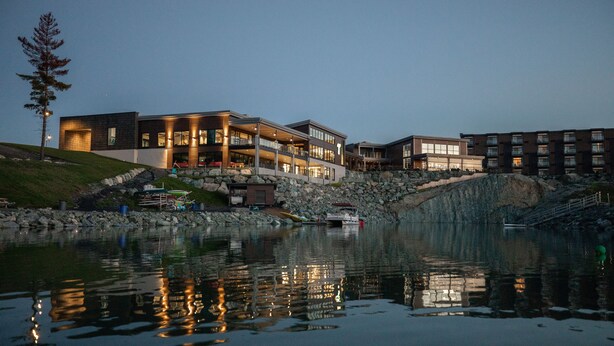 Un hôtel situé au bord de l’eau, avec plusieurs étages, des balcons et un mur de soutènement en pierre.
