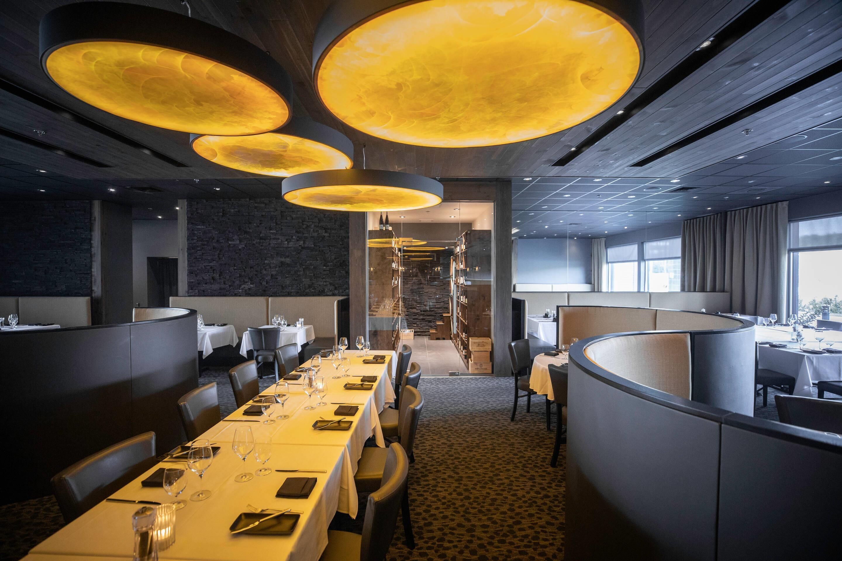 Un restaurant moderne avec des tables hautes, un éclairage encastré et un mur en pierre en arrière-plan.