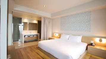 Una habitación de hotel moderna con una cama grande, un baño con espejo y tocador, y una obra de arte colgada en la pared.
