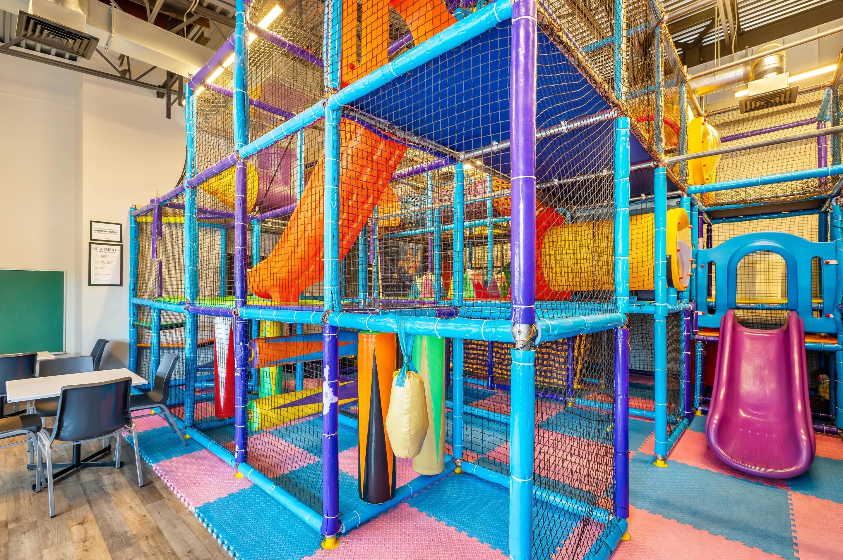A play area with a net structure, padded flooring, and a slide.