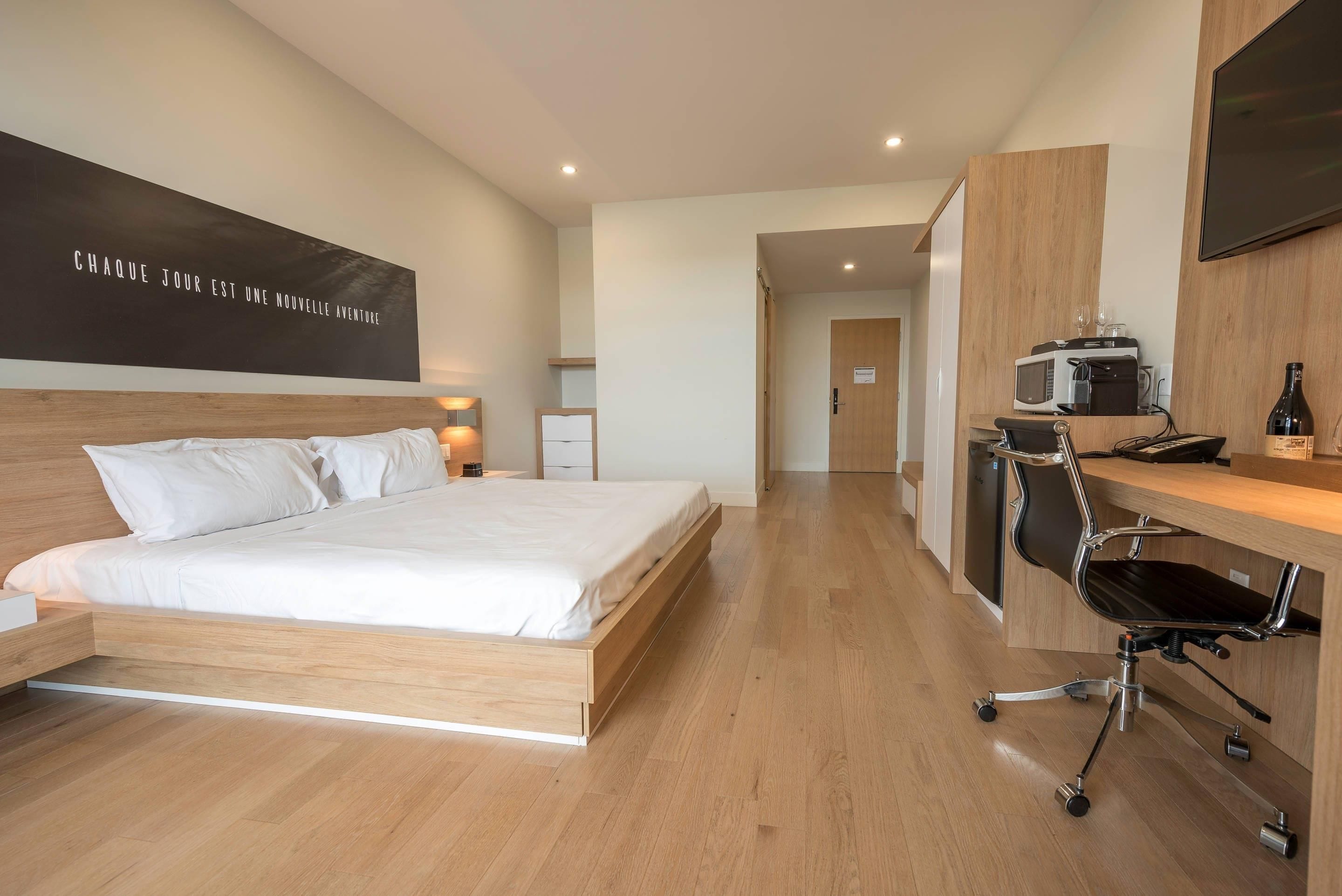 Una habitación de hotel moderna con una cama de madera, un escritorio con una silla, un microondas y un televisor.