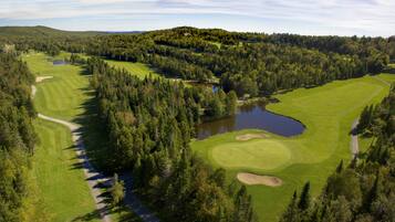 An aerial view of a golf course surrounded by dense forest, with multiple water bodies and a hilly landscape.